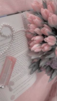 a bouquet of pink tulips sitting next to an open book with pearls on it