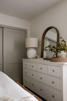 a bedroom with a dresser, mirror and vase on top of it in front of a bed