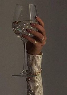 a woman's hand holding a wine glass in front of her face with glitter on it