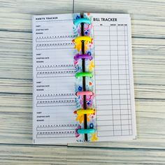 a binder with colorful clips attached to it on top of a wooden table next to a pen