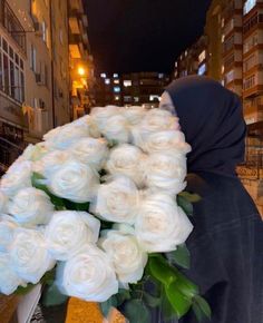 a person in a black hoodie is holding a bouquet of white roses on the street