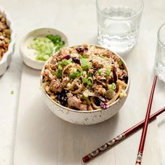 two bowls filled with food next to chopsticks on a white tablecloth and water glasses