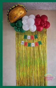 a party decoration with balloons, streamers and a taco hat on it's head