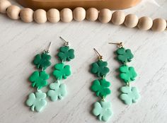 three pairs of green shamrock earrings on a table next to beads and a bead necklace