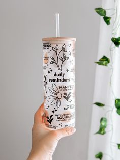 a person holding up a drink in front of a window with plants on the outside