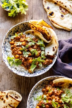 two bowls filled with food on top of a wooden table next to pita bread