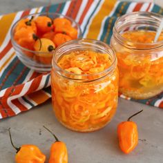 three jars filled with orange colored candy sitting on top of a table next to small peppers