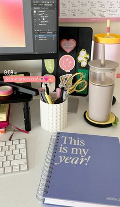 a desk with a computer, keyboard and planner