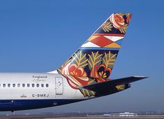 the tail end of an airplane painted with colorful designs on it's side, against a clear blue sky