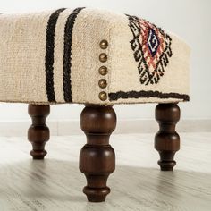 an upholstered bench with wooden legs and a multicolored rug on it