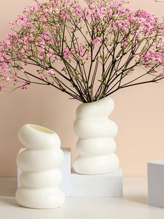 two white vases with pink flowers in them on a table next to each other