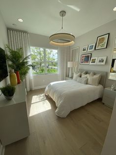 a bedroom with white bedding and pictures on the wall, along with potted plants