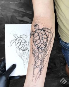 a person with a tattoo on their arm holding a piece of paper next to a drawing