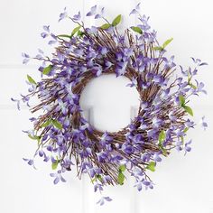 a wreath with purple flowers hanging on a white door