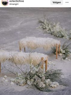 some white sheep are standing in the snow with flowers and plants around them on wooden posts