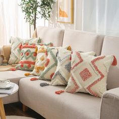 a couch with pillows on top of it in front of a potted plant and window