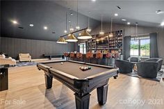 a pool table in the middle of a living room with chairs and lamps hanging from the ceiling