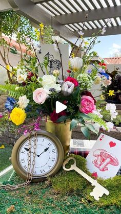 an arrangement of flowers, cards and a clock on the ground in front of a gazebo