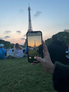 someone holding up their cell phone to take a photo in front of the eiffel tower