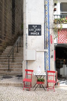 two red chairs sitting next to each other near a building with stairs leading up to it