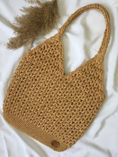 a crocheted bag with a feather on the side sitting on a white sheet