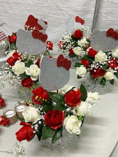 red and white flowers are arranged in vases on a table with silver heart shaped centerpieces