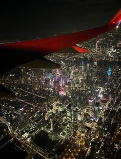 an airplane wing flying over a large city at night with the lights on and buildings lit up