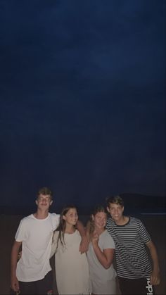 four young people standing on the beach at night with an airplane in the sky above them