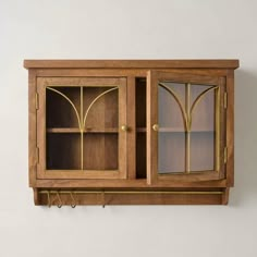 a wooden cabinet with glass doors and gold trimmings on the front, against a white wall