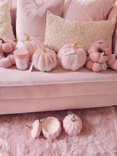 a pink couch with pillows and candles on it in front of some pumpkins that are sitting on the floor