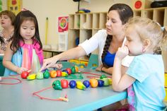 two girls and an adult are playing with toys at a table in a school room