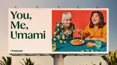 two women sitting at a table eating food from a bowl on top of a billboard