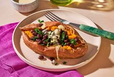 a white plate topped with a stuffed sweet potato filled with beans and veggies