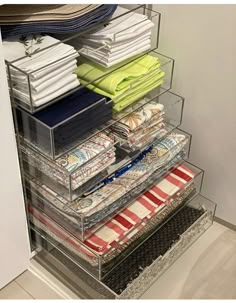 an organized closet with folded towels and folded shirts in clear acrylic boxes on the bottom shelf