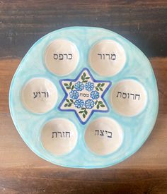 a blue plate with seven bowls and the names of different languages in hebrew on it