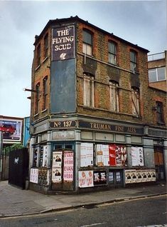 an old brick building on the corner of a street in front of buildings with signs and advertisements