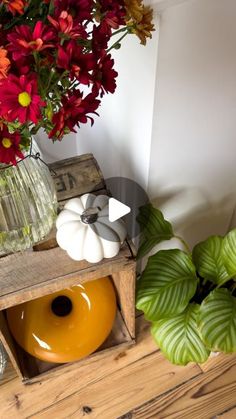 a vase filled with flowers sitting on top of a wooden box next to a potted plant