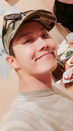 a young man wearing a hat and sunglasses smiles at the camera while standing in front of plates of food