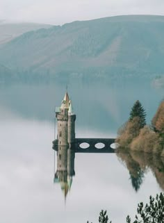 a castle sitting on top of a lake surrounded by trees and mountains in the background