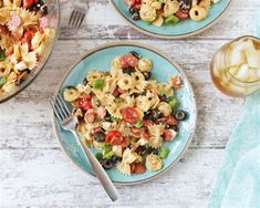 pasta salad with olives, tomatoes, and peppers on two plates next to a glass of wine