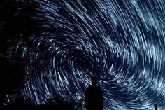 a man standing on top of a hill under a night sky filled with star trails