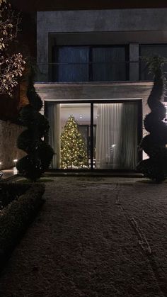 a christmas tree is lit up in front of a house at night with lights on