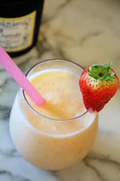 a glass with a straw and a strawberry on the rim, sitting on a marble table