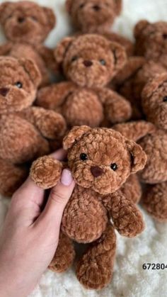 a hand holding a small brown teddy bear in front of a group of smaller brown teddy bears