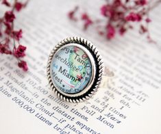 a map ring sitting on top of an open book next to pink flowers and branches