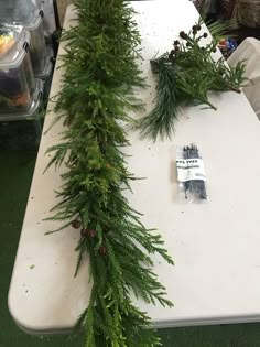 a white table topped with lots of green plants and pine cones on top of it