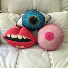 three pillows with different designs on them sitting on a white leather couch in front of an eyeball