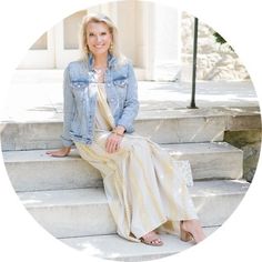 a woman sitting on the steps in front of a building wearing a dress and denim jacket