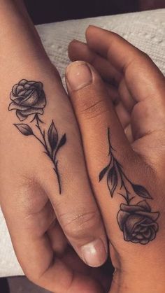 two people holding hands with tattoos on their fingers and one has a rose tattooed on it