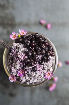 a glass bowl filled with blueberries and purple flowers on top of a gray surface